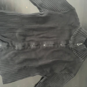 Svart ribbad kofta - Snygg svart ribbad kofta med dragkedja framtill. Perfekt för kyligare dagar med sin höga krage och långa ärmar. Ett stilrent plagg som passar till det mesta. PRIS KAN DISKUTERAS 