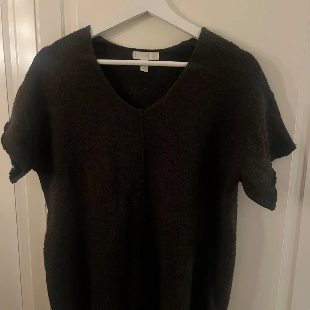 Säljer en mörkgrå tröja från H&M med korta ärmar och v-ringning. Perfekt för en stilren och enkel look. Tröjan är i ett mjukt material som känns skönt mot huden.. Neuletakit & Villapaidat.