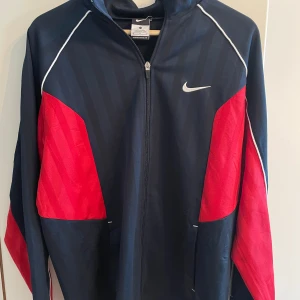 Vintage träningströja från Nike - Säljer en mörkblå och röd vintage träningströja från Nike med dragkedja och vita detaljer.  Strl M. Fint skick, inga anmärkningar. Hör av dig vid frågor.