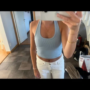 Ljusblå ribbad linnetopp - Säljer en superfin ljusblå ribbad linnetopp. Den är ärmlös och har en tight passform som är perfekt för sommaren. Toppen är croppad och ger en snygg look tillsammans med höga jeans eller shorts.