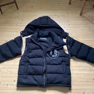 Corvidae puffer jacket - Corvidae puffer jacka med justerbara armar och huva. Man kan göra den till en väst eller en jacka. Storlek S. Skicket på jackan är bra/helt ok. Nypris är 2200 kr
