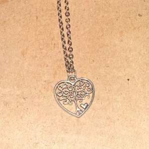 Silverhalsband med hjärthänge - Säljer ett superfint silverhalsband med ett hjärthänge. Hänget har ett intrikat trädmotiv med små detaljer och en liten hjärta i hörnet. Perfekt för att ge en romantisk touch till din outfit! 💖