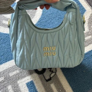 Ljusblå quiltad handväska från Miu Miu - Säljer en superfin ljusblå handväska från Miu Miu. Den är quiltad och har en snygg dragkedja upptill. Perfekt för att ge en touch av lyx till din outfit!