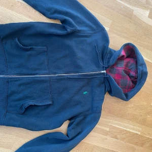 Polo ralph lauren zip hoodie - Nu säljer jag en riktigt unik polo ralph lauren tröja, en lite äldre modell som inte säljs längre. Tröjan är svart med ett grönt märke och så med ett röd/brunt randigt foder i luvan. Använd men fof bra skick, har små defekter, kom priv för mer info🤝