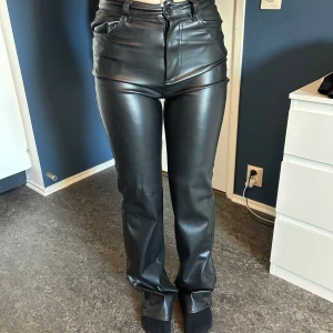 Svarta skinnbyxor från BikBok - Säljer ett par snygga svarta skinnbyxor från BikBok. De är högmidjade och har en tight passform som ger en cool look. Byxorna har en dragkedja och knapp framtill. Storlek 34