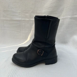 Svarta stövlar - Svarta stövlar med spänne. Funkar perfekt för någon med bredare fötter och större vader. Innersula mått: 25 cm. Klack: 3 cm. Total höjd: 26 cm. Bredd upptill: 37 cm runt + stretchband 🖤