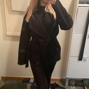 Svart kort kappa med knytband - Jääätttefin kappa med knytband. Den är så elegant och fin och man ser alltid uppklädd ut när man har den. Storlek 34 men passar 36.Jag köpte jackan för två vintrar sen så använd men fortfarande i bra skick, lite nopprig. Nypris 669kr🥰🥰