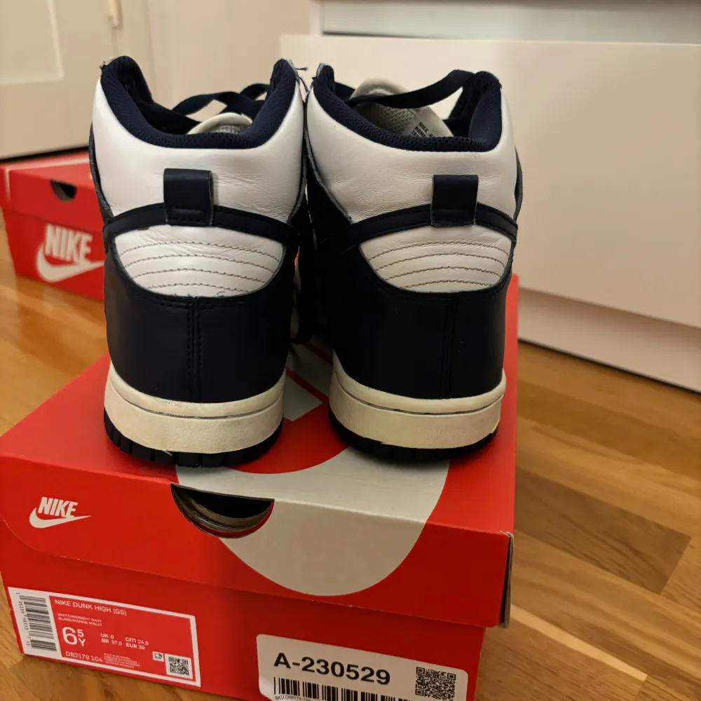 Säljer ett par Nike Dunk High sneakers i klassisk marinblå och vit färgkombination. Skorna har en hög siluett med snörning och är i bra skick med några defekter.. Skor.