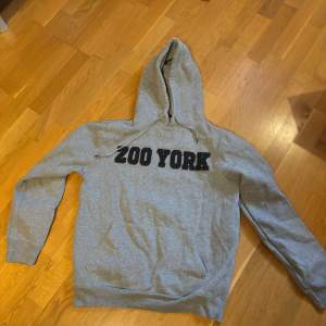 Säljer en grå hoodie från Zoo York i bra skick. Den har en klassisk design med svart text på bröstet och en bekväm huva. Perfekt för vardagsbruk.. Passar bra till jeans eller joggers 