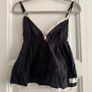 Odd Molly linne med spetsdetaljer - Säljer ett svart linne från Odd Molly med fina spetsdetaljer i vitt. Linnet har smala axelband och en söt rosett framtill. Perfekt för sommardagar eller som ett lager under en kofta. Använd men i bra skick!