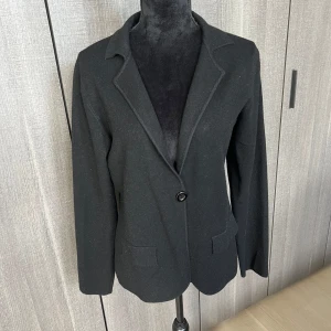 Svart stickad kavaj med knapp - Snygg svart stickad kavaj i klassisk stil med en knapp framtill. Perfekt för både vardag och fest. Den har långa ärmar och två fickor fram. Passar bra till höst och vår.