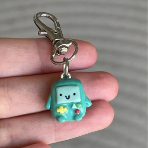 Turkos nyckelring med söt figur - En supergullig turkos nyckelring med en liten figur som har ett glatt ansikte. Perfekt att fästa på väskan eller nycklarna för en extra touch av personlighet. Figuren har små detaljer i gult och rött som gör den ännu charmigare. Nyckelringen är cirka 4 cm lång inklusive karbinhaken.