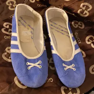 Säljer ett par snygga blå ballerinaskor från Adidas i mocka med vita detaljer. De har en söt snörning framtill och de klassiska tre ränderna på sidan. Perfekta för en avslappnad sommarlook eller en dag på stan. Skorna är i bra skick och redo för nya äventyr! 💙