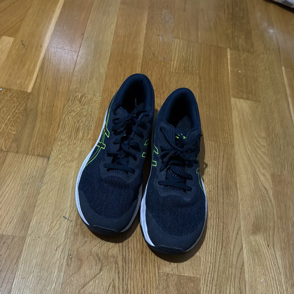 Säljer ett par svarta Asics träningsskor med gröna detaljer. Skorna har en bekväm passform och är perfekta för löpning eller gymträning. De har snörning och en slitstark sula för bra grepp. Använda men i bra skick!. Skor.