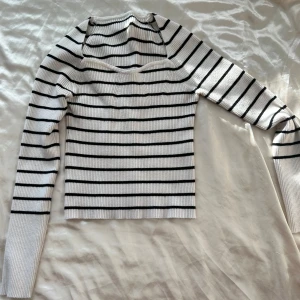 Vit och svart randig ribbad tröja - Säljer en superfin vit och svart randig tröja med ribbad struktur. Den har en unik cut-out detalj vid halsen. Tröjan är långärmad och passar perfekt för både vår och höst. Perfekt för att styla med jeans eller kjol!
