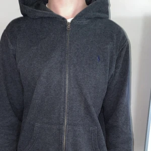 Polo Ralph lauren hoodie (grå) - Jag säljer en fet mörkgrå polo hoodie, den är en lite äldre modell och är lite uttöjd så den passar bra som M/L, jag är 180 och den är lite för liten för mig så därför jag säljer denna, den har en liten fläck på ryggen men går nog att få bort! Skicka dm vid intresse, priset kan diskuteras vid snabb affär!