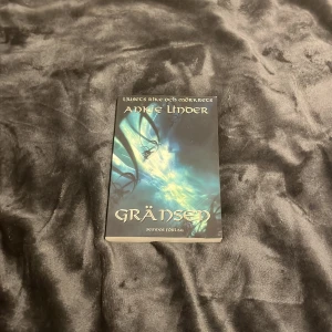 Gränsen - Boken 'Gränsen' av Annie Linder är en del av serien 'Ljusets rike och mörkrets'. Omslaget har en mystisk och magisk känsla med blå och gröna toner som skapar en drömliknande atmosfär. Perfekt för fantasyälskare som vill försvinna in i en annan värld.