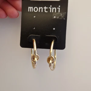 Guldiga örhängen från Montini - Säljer ett par snygga guldiga hoop-örhängen från Montini. De har en stilren design med en liten knutdetalj framtill. Perfekta för att piffa upp vilken outfit som helst! Oanvända.