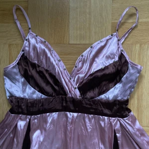 Lila och brun långklänning - Vintage ljusrosa och brun långklänning. Klänningen har smala justerbara axelband, dragkedja i sidan och fina detaljer vid bysten. 