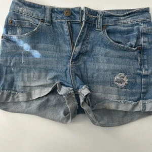 Jeans shorts - Fina jeans shorts med design på fickan. Säljer då de är för små och vill bli av med det.