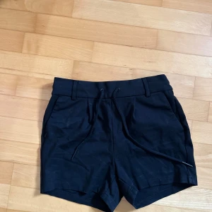 Svarta shorts med snörning - Säljer ett par snygga svarta shorts med snörning i midjan. De har en normal passform och är perfekta för sommaren. Shortsen har fickor på sidorna och är gjorda i ett bekvämt material.