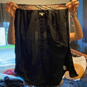 Svart skjorta från Burberry - Säljer en snygg svart skjorta från Burberry. Den har ett klassiskt rutigt mönster på insidan av kragen som ger en stilren touch. Perfekt för både vardag och fest! 🖤 !OBS! Det står storlek L men den sitter som en S