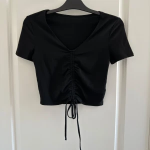 Svart och vit kortärmad topp med knyt - Säljer två snygga toppar i svart och vitt. De är kortärmade och har en v-ringad design med knytning framtill som ger en cool rynkad effekt. Perfekt för både vardag och fest! Båda för 50kr!