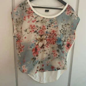 Blus - T-shirt blus med silkig, blommig framsida.