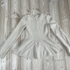 Vit ribbad tröja från H&M - Säljer en superfin vit ribbad tröja från H&M. Den har en peplumdesign som ger en snygg siluett och är perfekt för både vardag och fest. Tröjan är långärmad och gjord i ett mjukt material som känns skönt mot huden. Passar perfekt till jeans eller kjol!