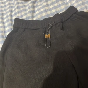 Svarta mjukisbyxor med snörning - Säljer ett par svarta mjukisbyxor i storlek L. De har en bekväm passform med elastisk midja och snörning för justering. Perfekta för en avslappnad dag hemma eller en snabb tur till affären. Byxorna har en stilren design med ribbade detaljer vid bensluten.