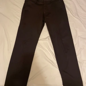NN. 07 Theo Klassisk Tailored Fit Chinos   - Säljer ett par eleganta och bekväma Theo klassisk tailored fit chinos i storlek 33/32. De är i brun färg. Byxorna är i mycket gott skick och knappt använda, utan några synliga märken eller slitage. Nypriset för dessa chinos var 1600 SEK.