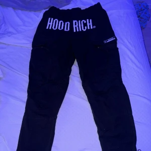 Svarta mjukisbyxor från Hoodrich - Säljer ett par svarta mjukisbyxor från Hoodrich i storlek XS. Byxorna har en elastisk midja med snörning och texten 'HOOD RICH' tryckt både fram och längs benet. Perfekta för en avslappnad och baggy stil!