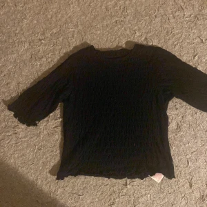 Svart topp från Name It - Säljer en svart topp från Name It i storlek 158-164. Toppen har trekvartsärmar och en ribbad struktur som ger en snygg look. Perfekt för en avslappnad stil.