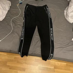 Svarta mjukisbyxor från Givenchy - Snygga svarta mjukisbyxor från Givenchy med vita detaljer längs sidorna. Byxorna har en bekväm passform med snörning i midjan och Givenchy-logga på benen. Perfekta för en avslappnad stil.