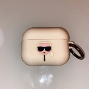 AirPods-skal från Karl Lagerfeld - Snyggt AirPods-skal från Karl Lagerfeld med Karls ikoniska figur med solglasögon 🕶️. Skalet har en praktisk nyckelring för enkel fastsättning på väskor eller annat. Fodralet har använts ett antal gånger och har även en liten repa längst ner till höger om skalet. Köpt för 299kr från Zalando. 