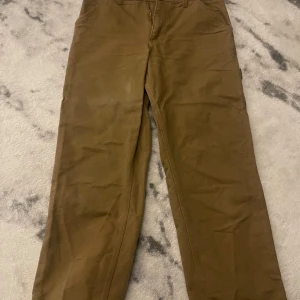  Carhartt byxor - Säljer ett par bruna byxor från Carhartt. De har en klassisk design med flera praktiska fickor och en robust känsla. Perfekta för en avslappnad stil eller arbete. Byxorna har en rak passform och är tillverkade i slitstarkt material. Storlek 30x32. Vid frågor om byxorna så ör det bara att skriva:)
