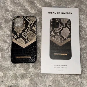 Mobilskal Midnight Python från Ideal of Sweden - Snyggt mobilskal från Ideal of Sweden i modellen Midnight Python. Skalet har ett coolt ormmönster i svart och beige med en krokodilliknande textur nedtill. Passar iPhone 11 Pro/XS/X. Mobilskalet är lite skadat i hörnet vilket man ser på bild 3. 