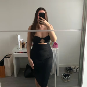 Svart tight klänning med cut-out detaljer - Snygg svart klänning med cut-out detaljer framtill. Klänningen är tight och har en elegant passform som framhäver figuren. Perfekt för en utekväll eller speciella tillfällen.