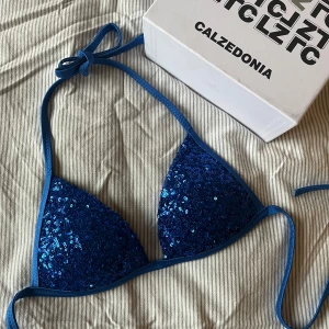 Blå-glittrig Calzedonia Cobey bikinitopp - Snygg blå bikiniöverdel från Calzedonia med glittrande paljetter. Den har knytband runt nacken och ryggen för justerbar passform. Den är helt ny och endast testad, så i perfekt skick!💕