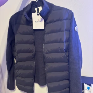 Moncler Cardigan Jacka - Helt ny Snygg grå/svart cardigan jacka  från Moncler med dragkedja och ribbade detaljer. Jackan har en quiltad design och Moncler-logga på ärmen. Perfekt för kyligare dagar. Passar både för vinter/vår/sommar/höst. Storlek Small säljs för 2800 men priset går att diskutera