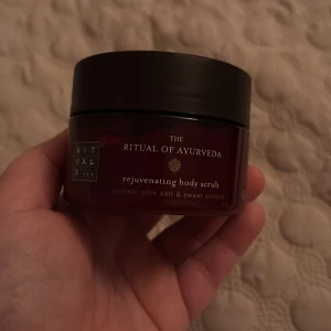 The Ritual of Ayurveda Rejuvenating Body Scrub - En lyxig kroppsskrubb från Rituals med doft av punjabi pink salt och sötmandel. Perfekt för att ge huden en mjuk och len känsla. Kommer i en elegant burk med mörkt lock.