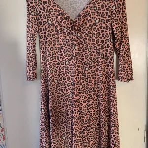 Leopardmönstrad klänning från Stockholms Klänningsfabrik - Snygg leopardmönstrad klänning i rosa och svart från Stockholms Klänningsfabrik. Klänningen har en v-ringad design med trekvartsärm och en smickrande passform. Litet hål i nacken efter prislapp. Stl T3, motsvarar ca 42