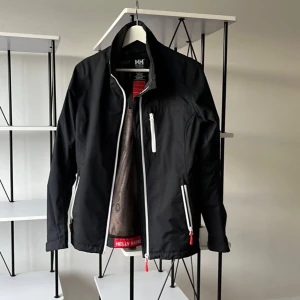 Svart jacka från Helly Hansen - Säljer denna jacka från Helly Hansen. Bra skick då den knappt är använd. Perfekt för både vardag och utomhusaktiviteter. Storlek M men sitter lite mindre så passar nog S också. Skriv gärna vid frågor!