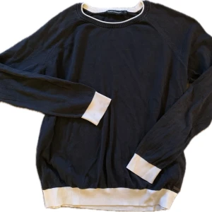 Svart tröja från peak performance  - Snygg svart tröja från peak performance med vita ribbade muddar vid ärmslut och nederkant + liten hals detalj. Perfekt för en stilren look. Tröjan har långa ärmar och rund halsringning.