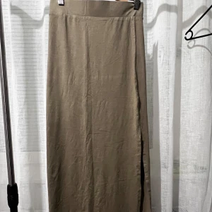 Beige långkjol med slits - Snygg beige långkjol med en diskret slits på sidan. Perfekt för en stilren och elegant look. Kjolen har en enkel design som gör den lätt att matcha med olika toppar.