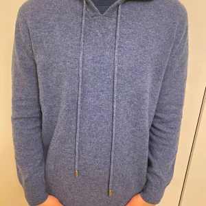 Merinoull hoodie Blå  - Säljer en snygg blå stickad hoodie med dragsko i huvan. Perfekt för kyliga dagar och ger en avslappnad stil. Passar bra till jeans eller chinos.