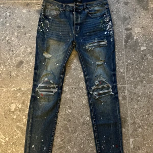 Blå jeans med slitningar från Amiri - Snygga blå jeans från Amiri med coola slitningar och färgstänk. De har en modern skinny passform och klassisk femficksdesign. Perfekta för en trendig look.