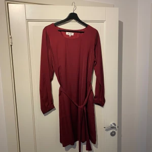 Vinröd klänning från Day Like - Snygg vinröd klänning från Day Like i storlek L. Klänningen har långa ärmar och ett knytband i midjan för en smickrande passform. Perfekt för höst och vinter med sin djupa färgton.