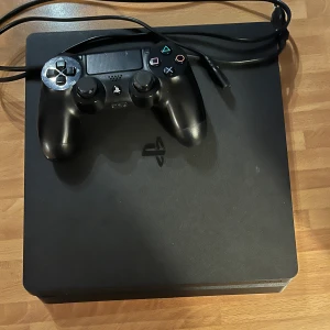 PlayStation 4 Slim med DualShock 4-kontroll - Säljer en PlayStation 4 Slim i svart med en DualShock 4-kontroll. Konsolen har en stilren design med det klassiska PlayStation-logot. Perfekt för gaming och underhållning.