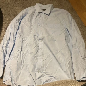 Ljusblå skjorta från Dressmann - Säljer en ljusblå skjorta från Dressmann i storlek 3XL. Skjortan har långa ärmar och knappar framtill. Bra skick, säljer för 175 men kan gå ner i pris. Skriv till mig för övriga frågor och bilder!